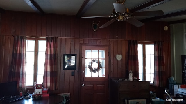 entryway with plenty of natural light, beam ceiling, and wood walls