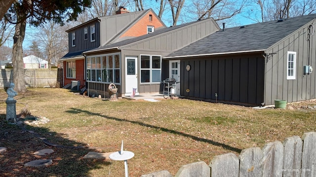 rear view of property featuring fence, a lawn, board and batten siding, and a sunroom