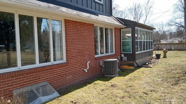 view of side of property with cooling unit, fence, a sunroom, board and batten siding, and brick siding