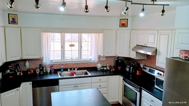 kitchen featuring dark countertops, under cabinet range hood, appliances with stainless steel finishes, white cabinetry, and a sink