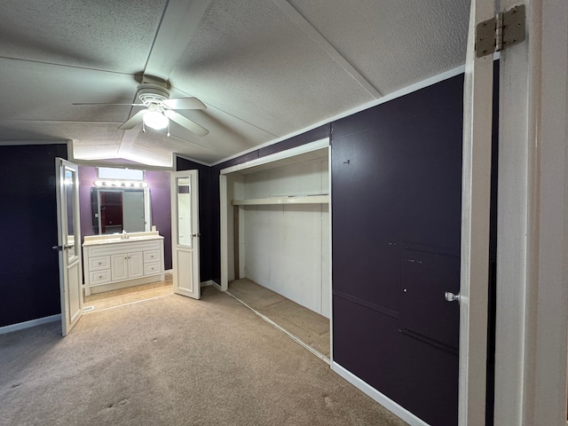 unfurnished bedroom featuring vaulted ceiling, ensuite bathroom, light carpet, a textured ceiling, and a closet