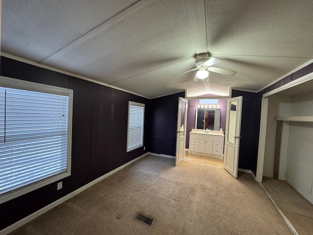 unfurnished bedroom with lofted ceiling, connected bathroom, light carpet, a textured ceiling, and ceiling fan