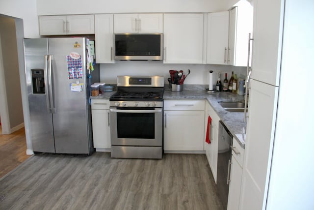 kitchen featuring white cabinetry, stainless steel appliances, hardwood / wood-style floors, and light stone counters