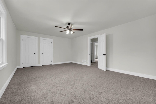 unfurnished bedroom featuring ceiling fan, carpet, and two closets