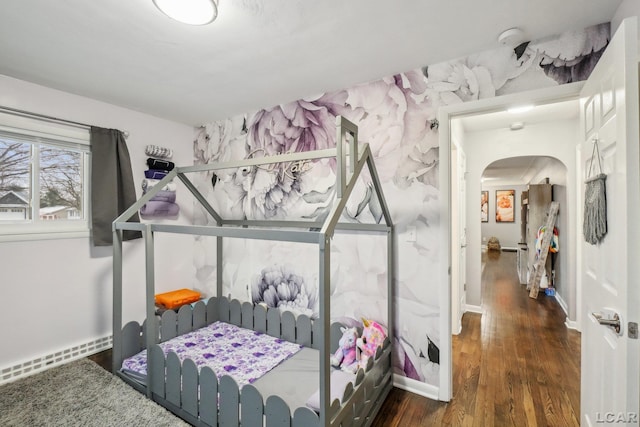 bedroom featuring wood finished floors, arched walkways, baseboards, and a baseboard radiator