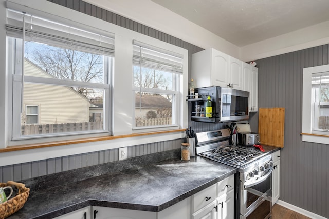 kitchen featuring white cabinets, wooden walls, dark hardwood / wood-style flooring, and appliances with stainless steel finishes