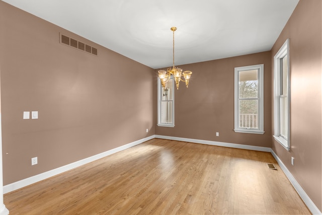 spare room featuring light wood-type flooring and a chandelier