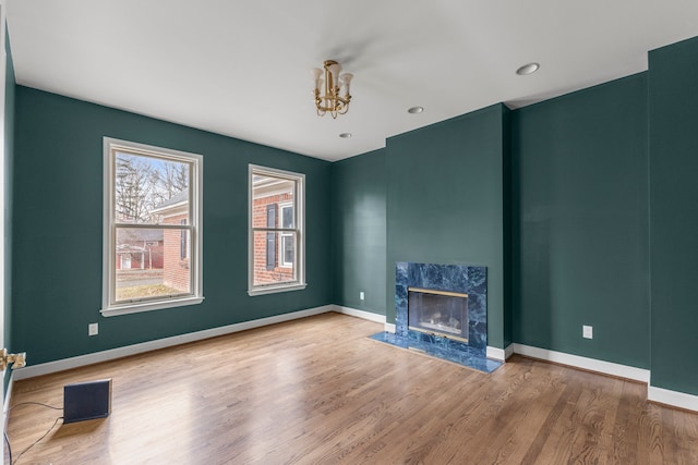 unfurnished living room with a high end fireplace, a chandelier, and wood-type flooring