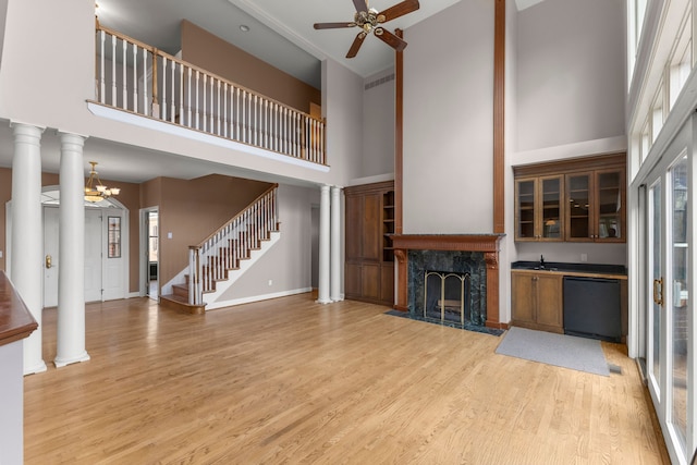 unfurnished living room with light hardwood / wood-style floors, a premium fireplace, decorative columns, and a towering ceiling