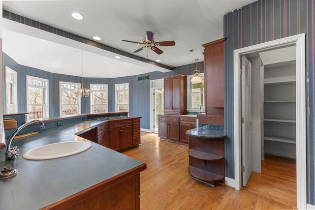 kitchen featuring light wood-type flooring, sink, ceiling fan with notable chandelier, and pendant lighting