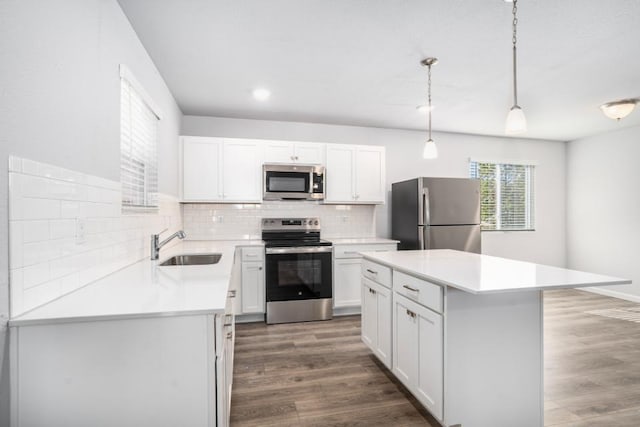 kitchen featuring sink, appliances with stainless steel finishes, white cabinetry, a kitchen island, and decorative light fixtures