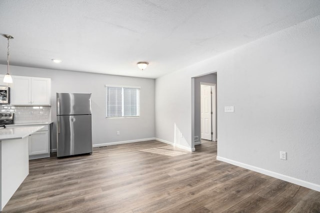 kitchen featuring appliances with stainless steel finishes, pendant lighting, white cabinetry, backsplash, and dark hardwood / wood-style flooring