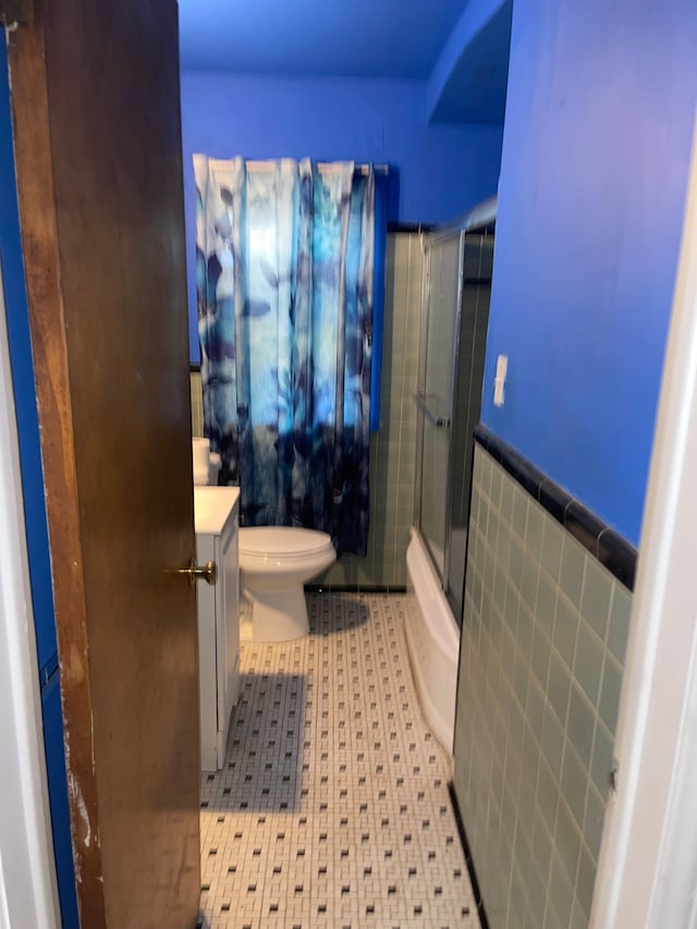 full bathroom featuring toilet, vanity, tile walls, and combined bath / shower with glass door