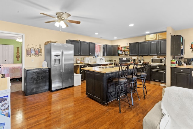 kitchen with a center island, ceiling fan, a kitchen bar, wood-type flooring, and stainless steel appliances