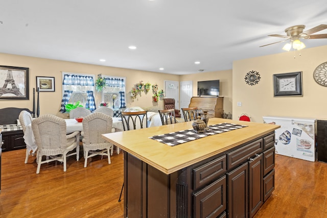 kitchen with a kitchen bar, dark hardwood / wood-style flooring, dark brown cabinets, ceiling fan, and a center island