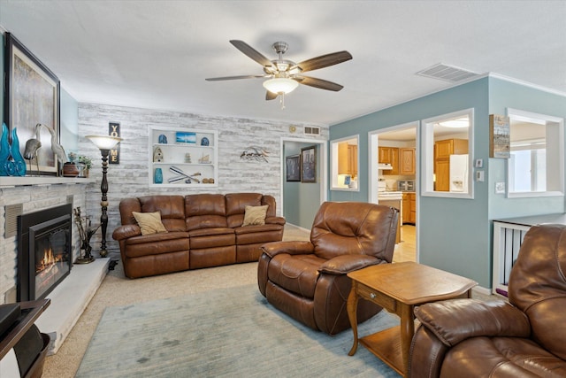 carpeted living room with ceiling fan, a stone fireplace, and built in shelves