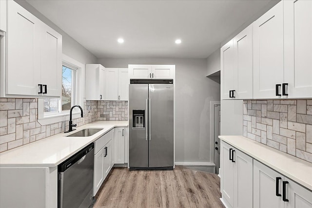 kitchen featuring sink, appliances with stainless steel finishes, white cabinetry, backsplash, and light hardwood / wood-style floors