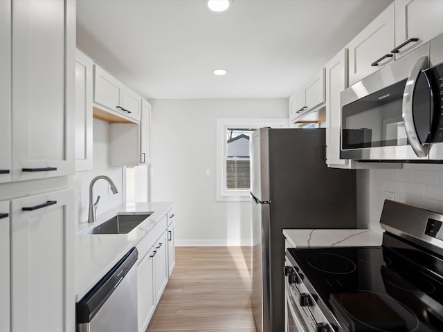 kitchen with white cabinets, sink, light stone countertops, light hardwood / wood-style floors, and stainless steel appliances