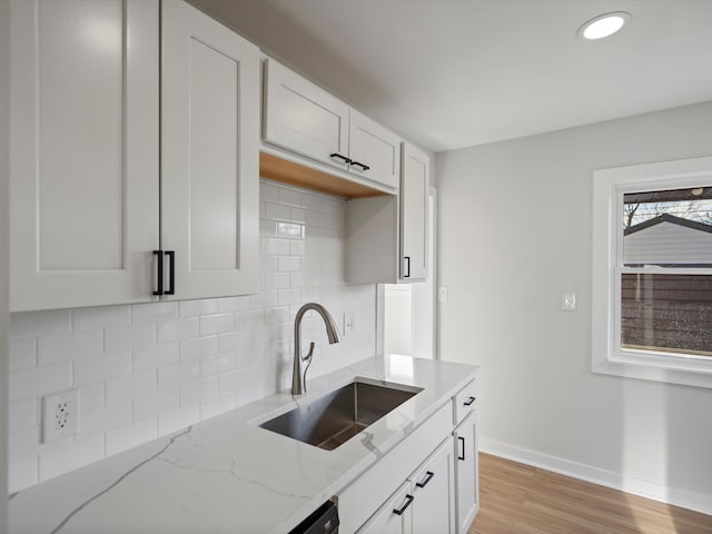 kitchen with backsplash, sink, light wood-type flooring, light stone counters, and white cabinetry