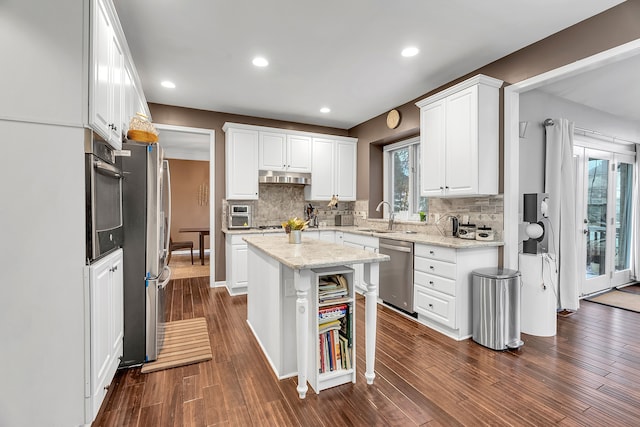 kitchen with light stone counters, stainless steel appliances, white cabinets, a kitchen island, and a sink