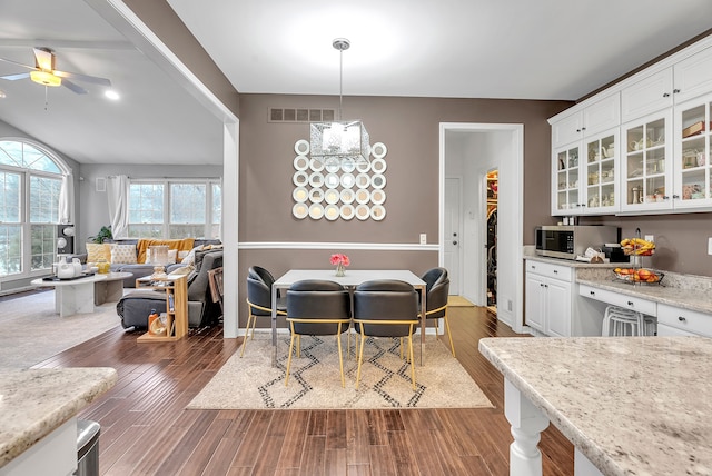 dining area with dark wood-style floors, visible vents, vaulted ceiling, and ceiling fan with notable chandelier