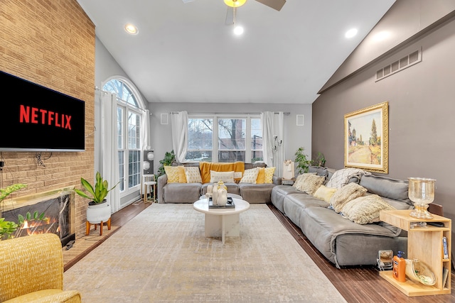 living room featuring high vaulted ceiling, a brick fireplace, wood finished floors, and visible vents