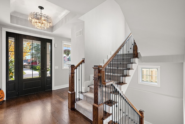 foyer with a raised ceiling, dark wood-type flooring, and a chandelier