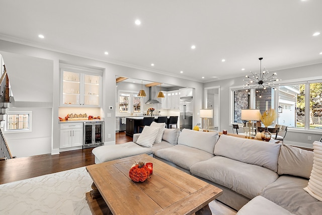 living room with a chandelier, dark wood-type flooring, beverage cooler, and ornamental molding