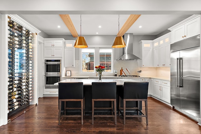 kitchen with beamed ceiling, white cabinetry, wall chimney range hood, and stainless steel appliances