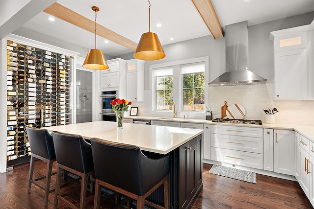 kitchen featuring beam ceiling, white cabinetry, wall chimney exhaust hood, a kitchen bar, and a kitchen island