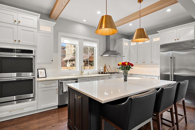 kitchen with sink, wall chimney exhaust hood, stainless steel appliances, beamed ceiling, and white cabinets