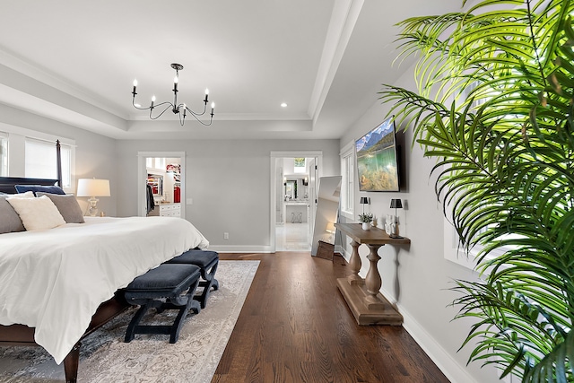 bedroom with dark hardwood / wood-style flooring, a walk in closet, a tray ceiling, an inviting chandelier, and connected bathroom