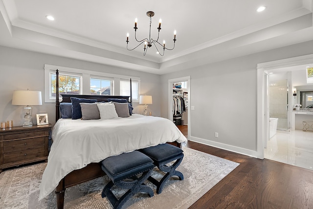 bedroom with a closet, a spacious closet, connected bathroom, and a tray ceiling