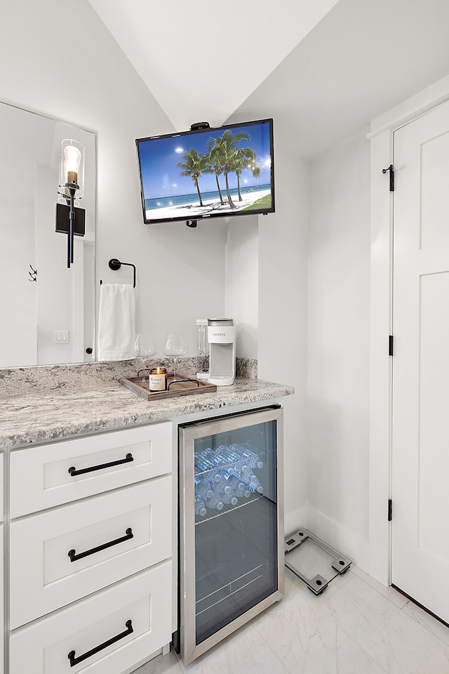 bar with white cabinets, light stone countertops, and beverage cooler