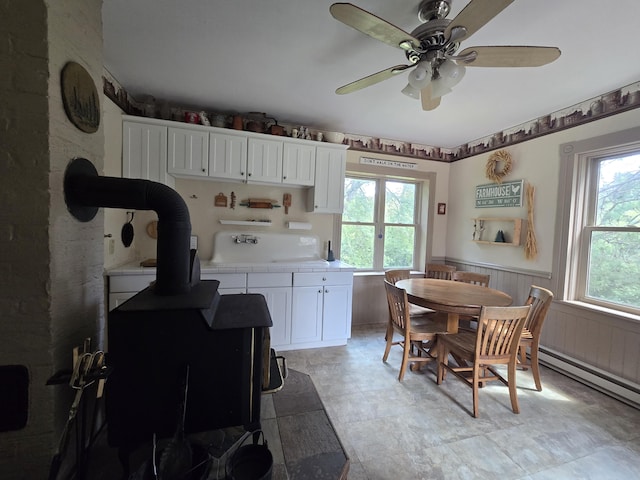 kitchen with white cabinets, ceiling fan, a healthy amount of sunlight, and a wood stove