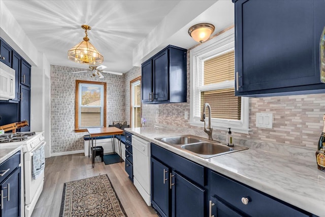 kitchen featuring blue cabinetry, white appliances, hanging light fixtures, and sink