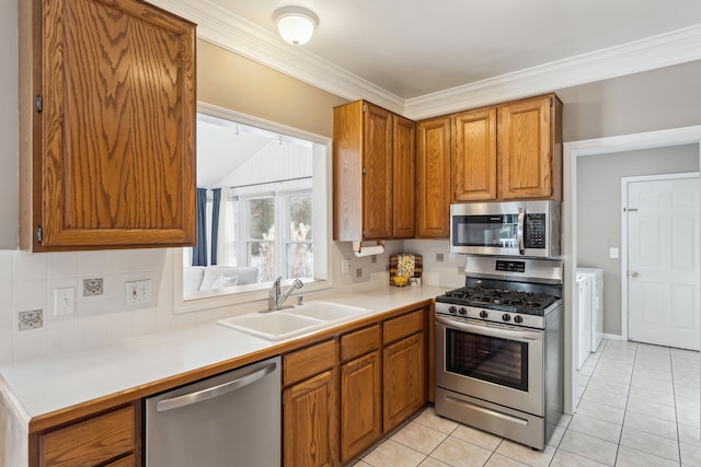 kitchen featuring sink, washing machine and dryer, crown molding, light tile patterned floors, and appliances with stainless steel finishes