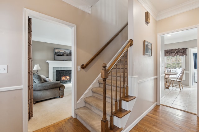 stairs with hardwood / wood-style floors, crown molding, and a tile fireplace