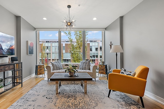 living room with a wealth of natural light, floor to ceiling windows, an inviting chandelier, and light hardwood / wood-style floors