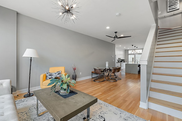 living room with ceiling fan with notable chandelier, sink, and wood-type flooring