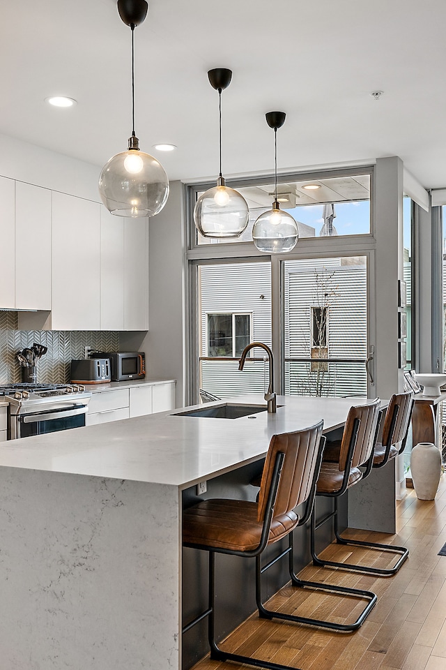 kitchen featuring sink, pendant lighting, stainless steel appliances, white cabinets, and a kitchen island with sink