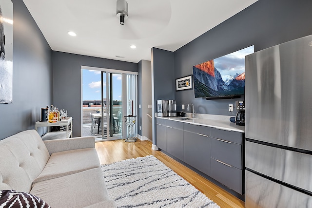 bar featuring sink, gray cabinetry, stainless steel refrigerator, and light wood-type flooring