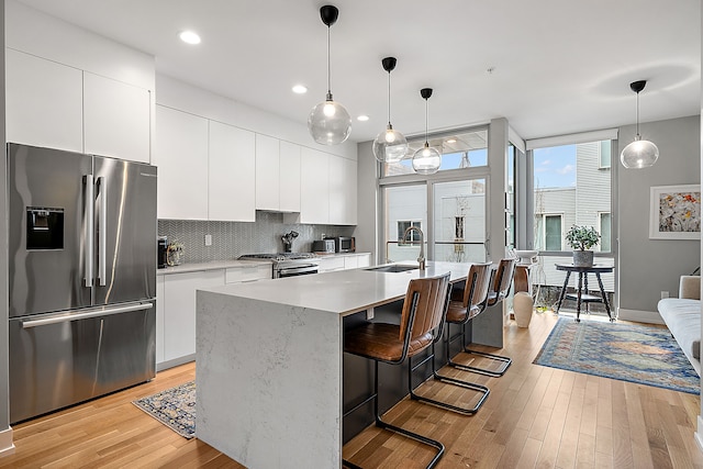 kitchen with sink, white cabinetry, stainless steel appliances, an island with sink, and tasteful backsplash