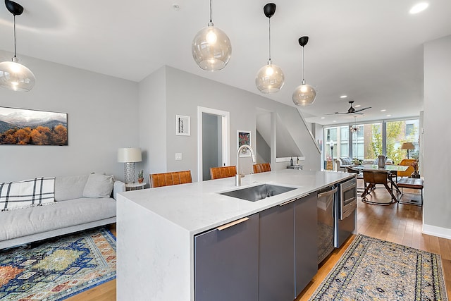 kitchen with sink, an island with sink, light hardwood / wood-style floors, and decorative light fixtures