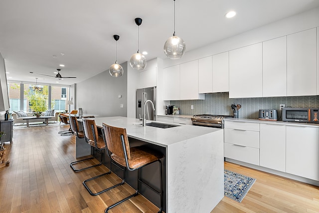 kitchen featuring sink, backsplash, stainless steel appliances, white cabinets, and an island with sink