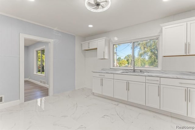 kitchen with light stone counters, white cabinetry, and sink