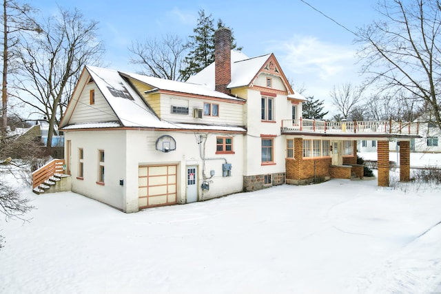 snow covered house featuring a balcony, an attached garage, metal roof, and a chimney