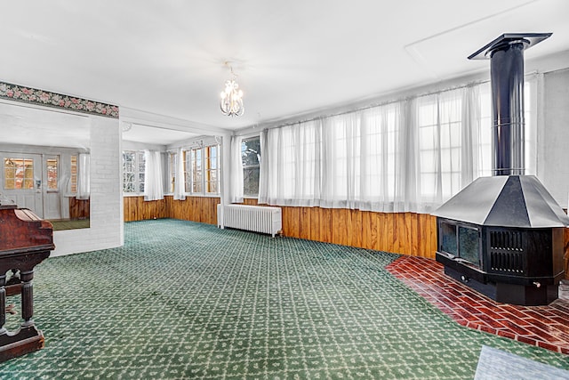 sunroom / solarium with a wood stove, a notable chandelier, a healthy amount of sunlight, and radiator heating unit