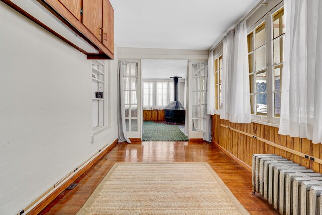 corridor with radiator heating unit, light hardwood / wood-style flooring, and wood walls