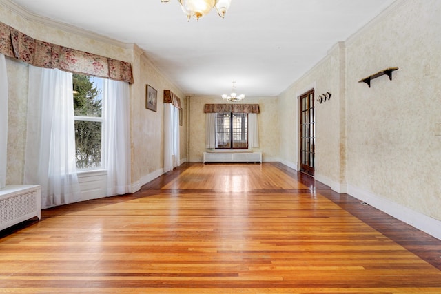 spare room with baseboards, radiator heating unit, ornamental molding, wood finished floors, and a notable chandelier